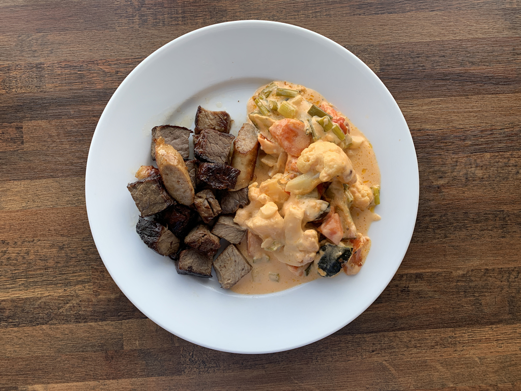 a plate with baked vegetables in cheese sauce and warmed up steak pieces